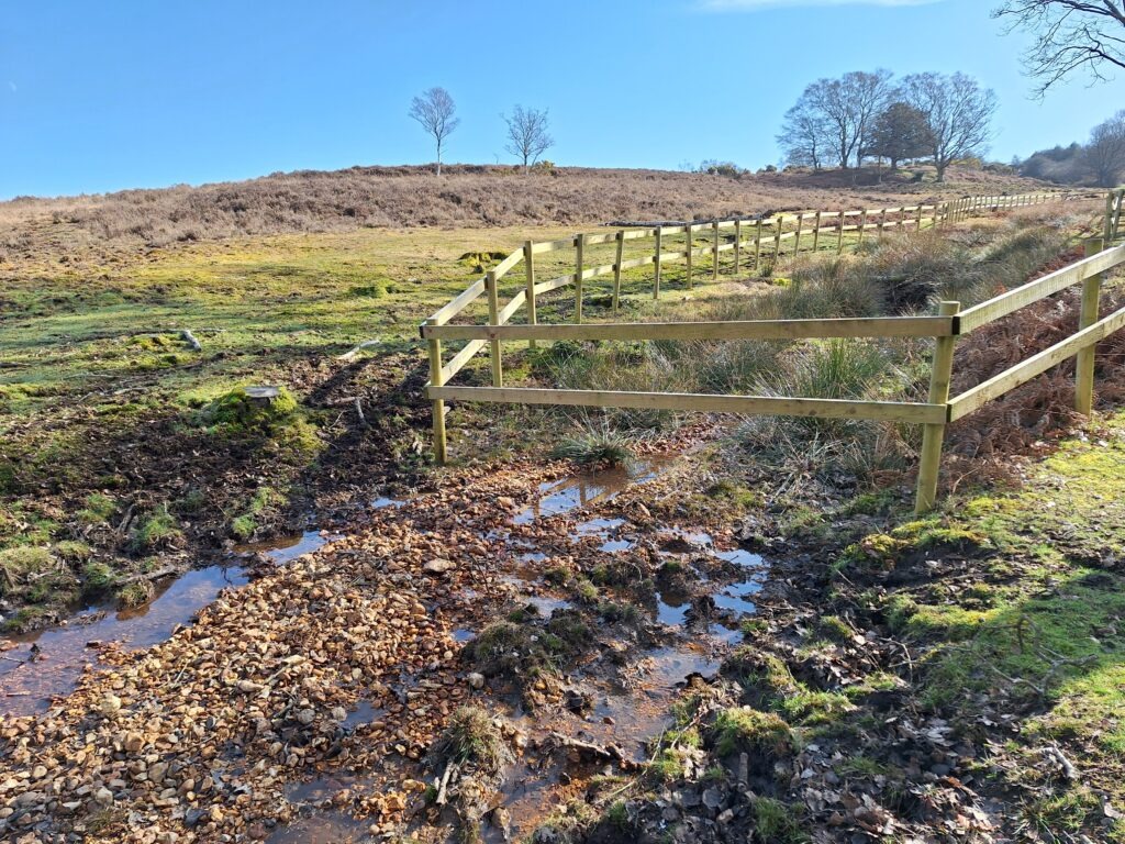 A muddy area partly surrounded by a fence