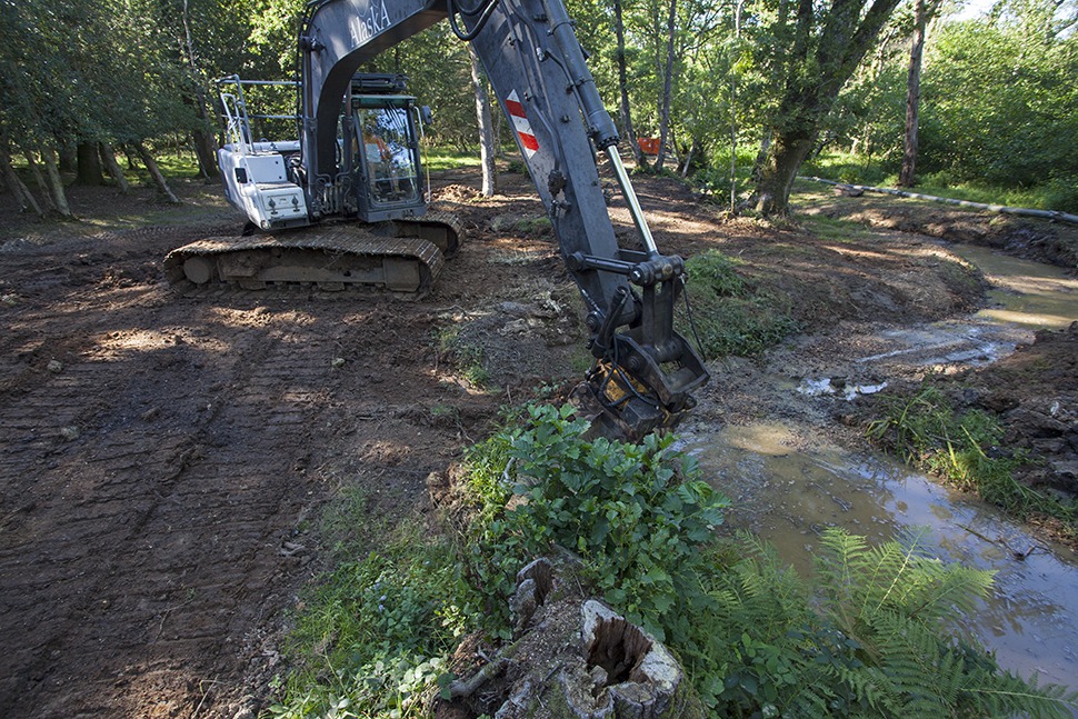 Excavator digging a new meandering stream channel during restoration work at Wootton, New Forest National Park, Hampshire, England