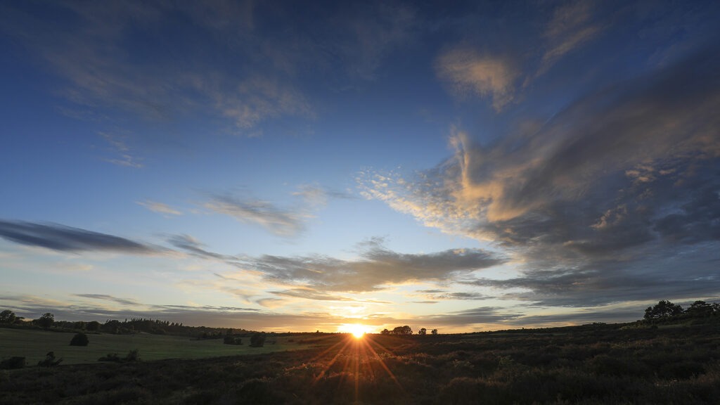 Sunset at Horseshoe Bottom with sunburst over rolling heathland and fields beneath a wide blue sky with scattered clouds